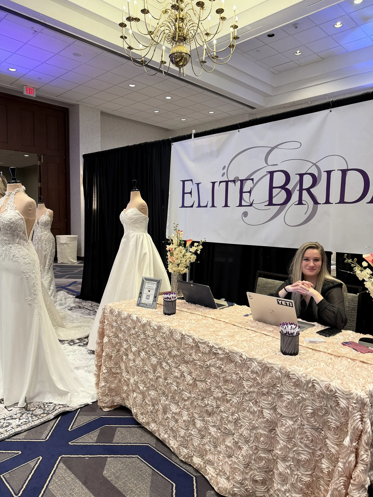 Elite Bridal booth with wedding gowns and rose-covered table