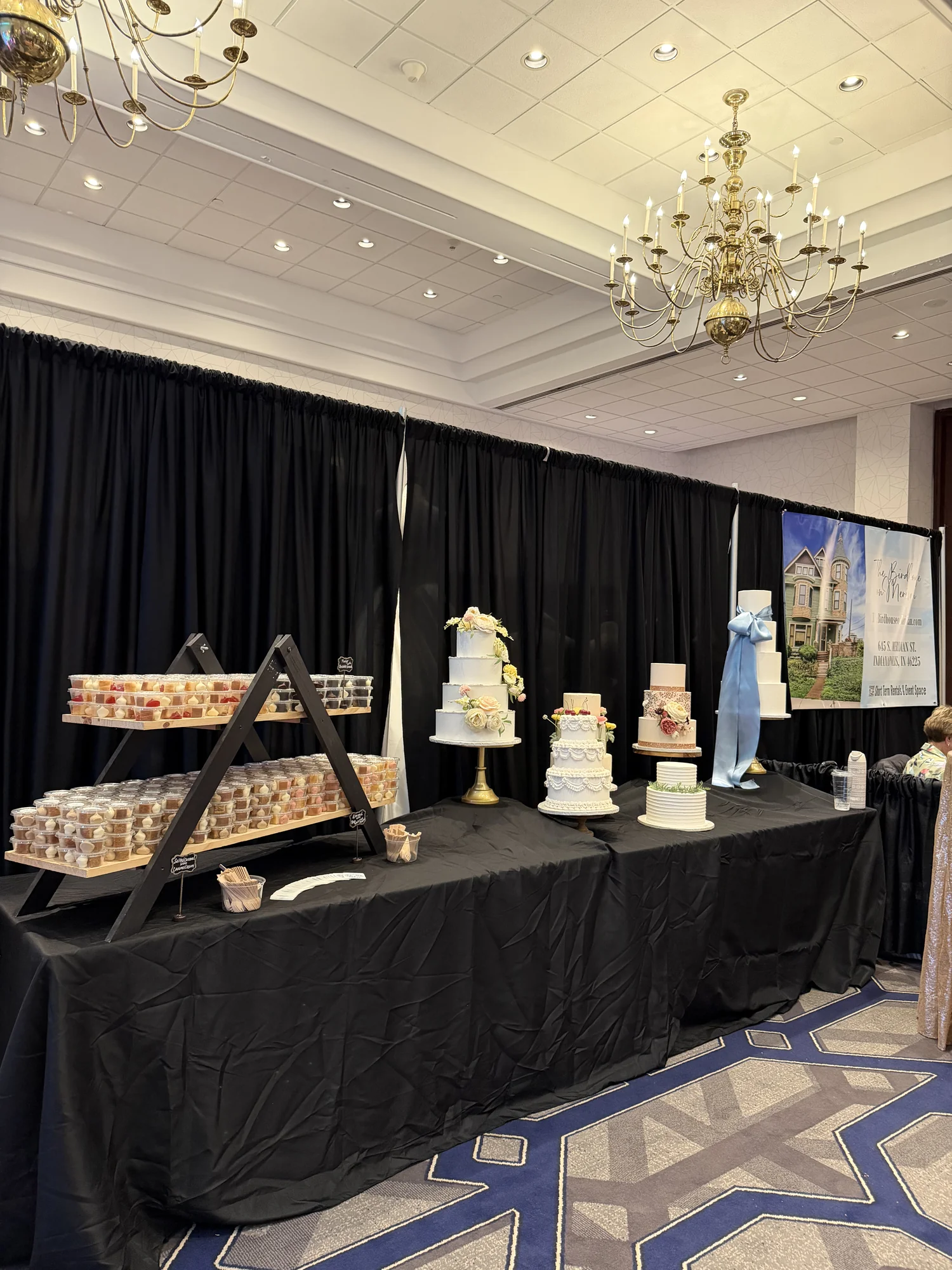 Wedding cake display with several tiered cakes on black linen under a chandelier
